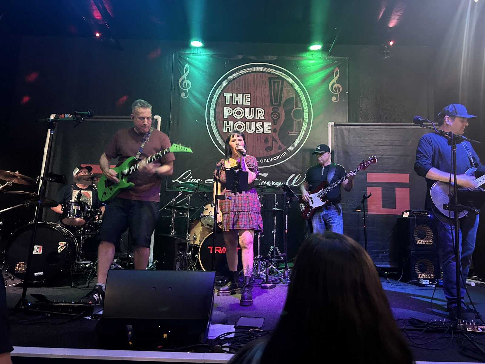your alternative at the pour house in paso robles, september 23, 2026: the full stage with the singer between guitarists, the drummer at left, and an audience member in front.
