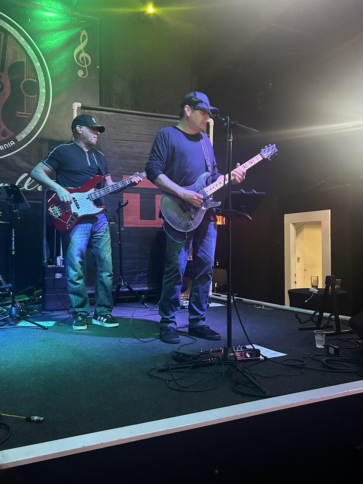 your alternative at the pour house in paso robles, september 23, 2026: a guitarist at a microphone on the right side of the stage, with another band member playing behind him.