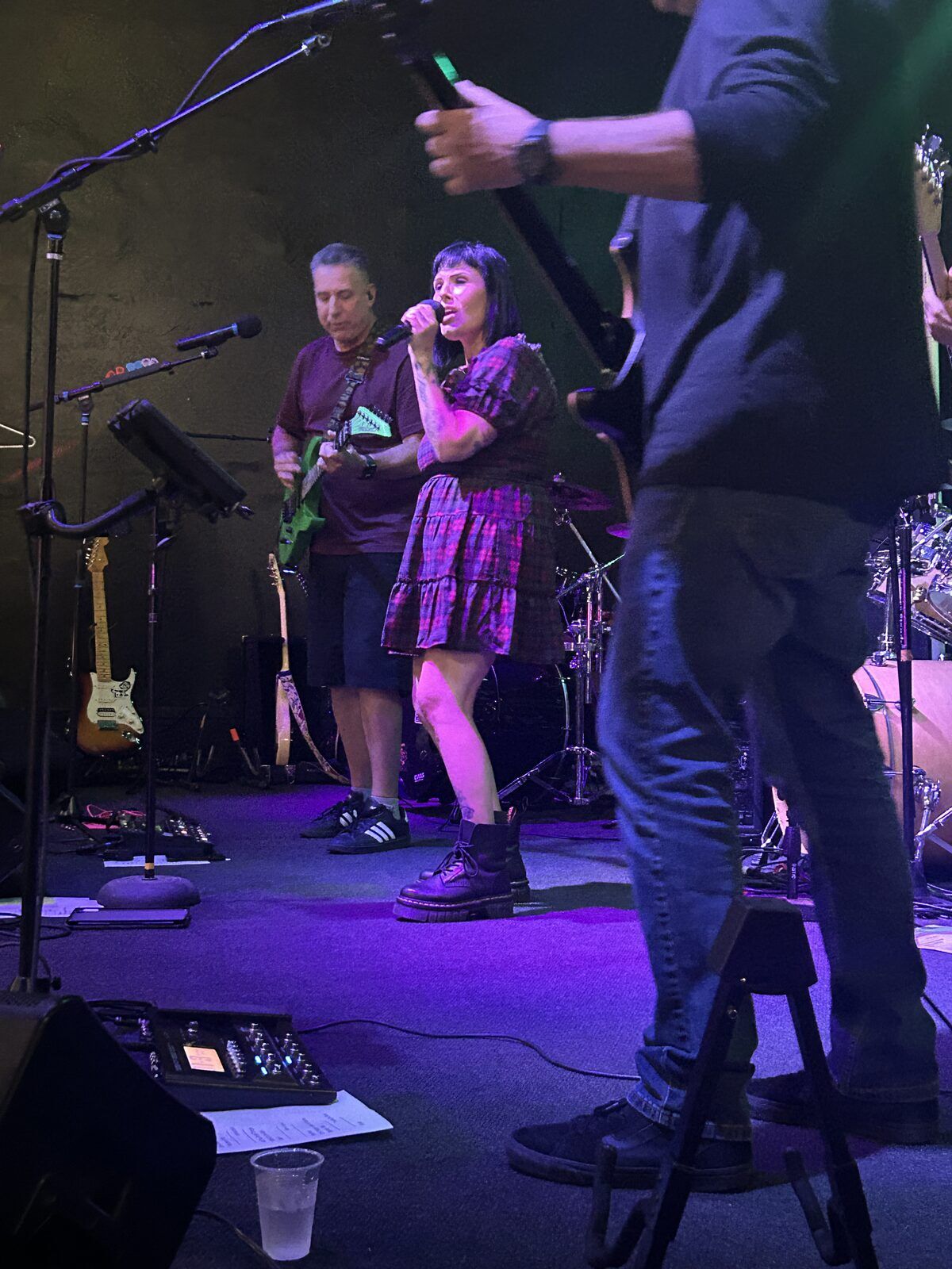 your alternative at the pour house in paso robles, september 23, 2026: a side-stage view of the singer at her microphone, with a guitarist in the foreground.